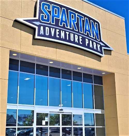 Sign for Spartan Adventure Park on a building with large glass doors and a clear blue sky above.