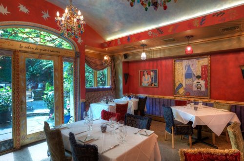 Cozy restaurant interior with colorful decor, elegant tables, and a view of a garden through large glass doors.