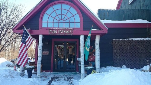 A cozy building entrance with a large window, American and state flags, surrounded by snow.