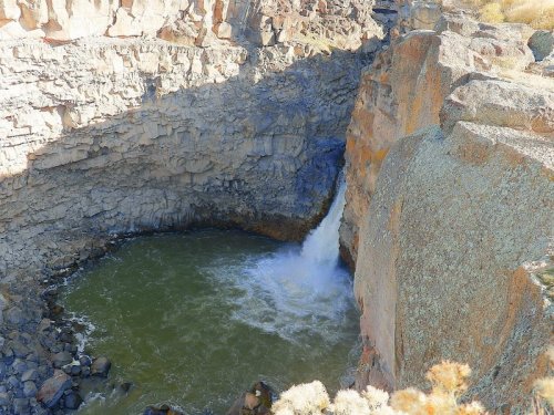 A waterfall cascades into a rocky pool surrounded by steep cliffs and rugged terrain.
