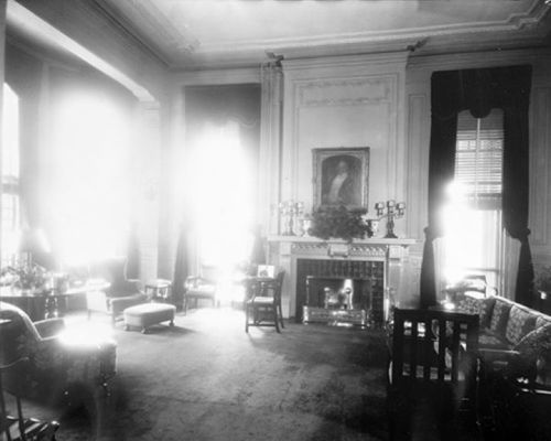 A vintage living room with elegant furniture, a fireplace, and large windows letting in bright light.