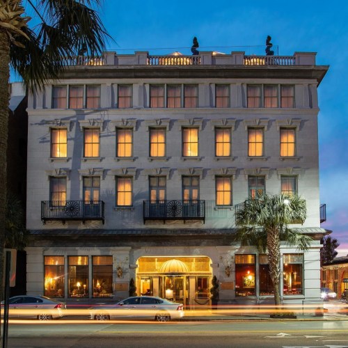 Historic building with illuminated windows, palm trees in front, and a twilight sky in the background.