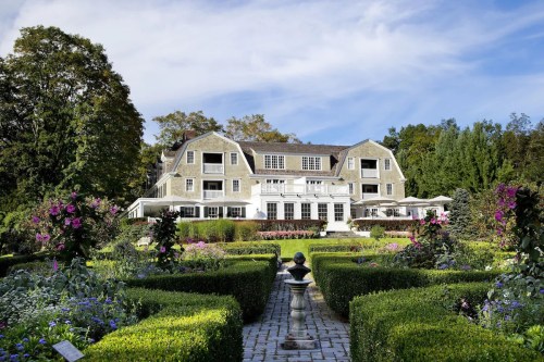A large, elegant house surrounded by lush gardens and colorful flowers under a clear blue sky.