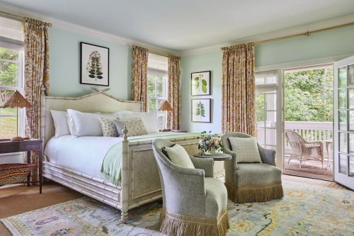 Bright and airy bedroom with a large bed, two chairs, floral curtains, and a view of a balcony.