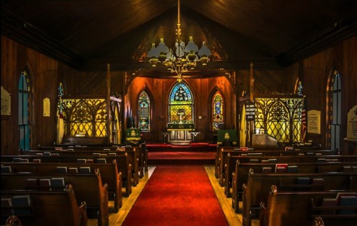 Interior of a church featuring stained glass windows, wooden pews, and a red carpet leading to the altar.