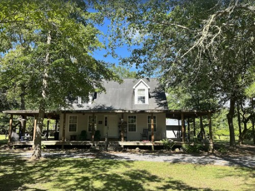 A two-story house with a porch, surrounded by trees and greenery under a clear blue sky.