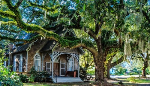 A charming wooden house with ornate details, surrounded by large trees draped in Spanish moss.
