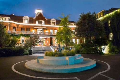 A beautifully lit historic building at night, featuring a central circular garden and surrounding greenery.