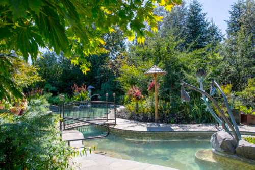 A serene garden with a pool, lush greenery, and a decorative gazebo surrounded by vibrant flowers and plants.