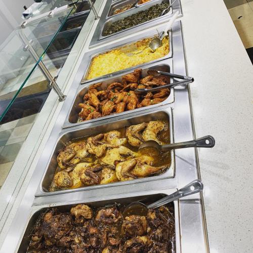 A buffet display featuring various dishes, including chicken, macaroni and cheese, and greens in metal trays.