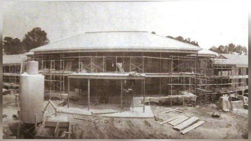 Black and white photo of a building under construction, surrounded by scaffolding and construction materials.