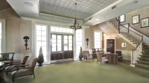 Elegant interior of a foyer with a staircase, seating area, and large windows, featuring decorative plants and lighting.