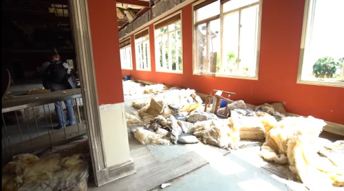 An abandoned room with insulation scattered on the floor and large windows letting in natural light.