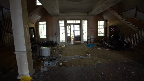 An abandoned interior with debris, broken furniture, and large windows, creating a desolate atmosphere.