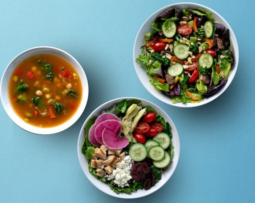 A colorful meal featuring two salads with greens, tomatoes, cucumbers, and a bowl of soup with vegetables and chickpeas.