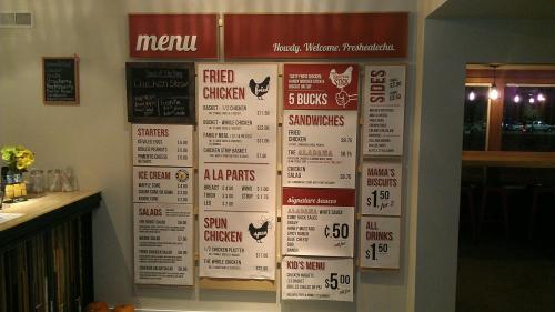 Menu board featuring fried chicken, sides, sandwiches, and kids' menu with prices listed. Welcoming atmosphere.