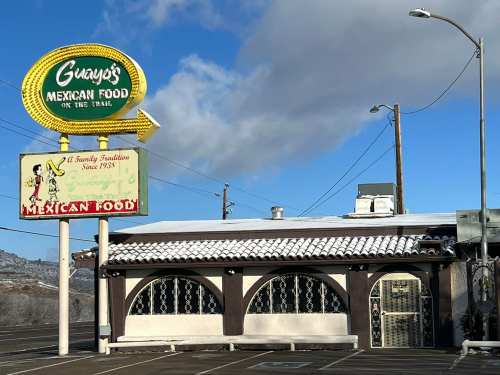 A Mexican restaurant with a colorful sign, featuring a snowy roof and a clear blue sky in the background.