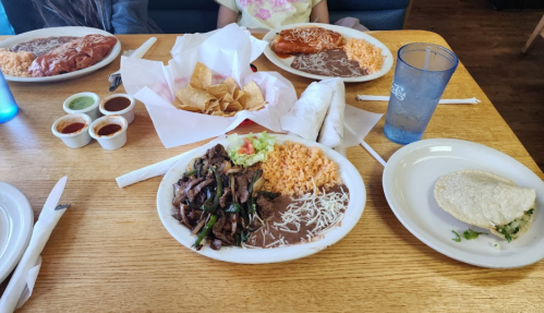 A table with two plates of Mexican food, including rice, beans, and a taco, alongside chips and sauces.