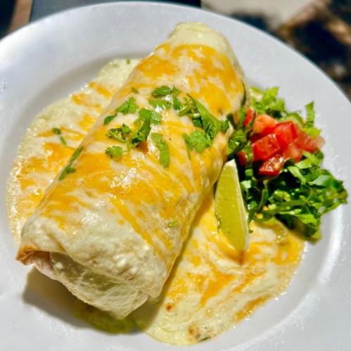 A delicious burrito topped with melted cheese, served with lettuce, tomato, and a lime wedge on a white plate.