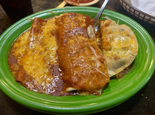 A vibrant green plate with two cheesy enchiladas covered in red sauce and a taco on the side.