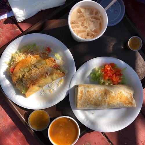 A tray with two plates: one with tacos topped with lettuce and cheese, the other with a burrito, plus sauces and a drink.