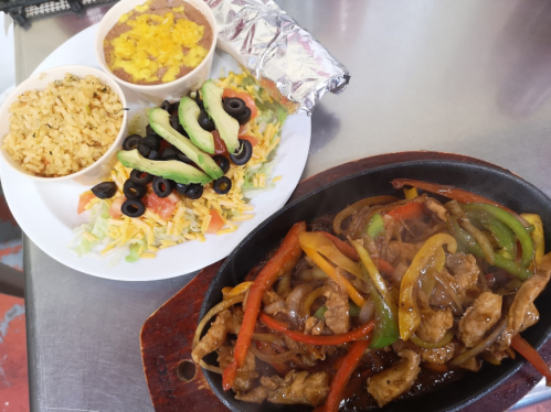 A sizzling platter of fajitas with colorful peppers, served with rice, beans, and a fresh salad on the side.