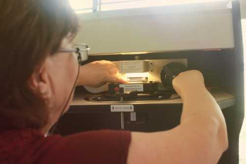 A person operates a film projector, adjusting the film inside while focused on the light source.