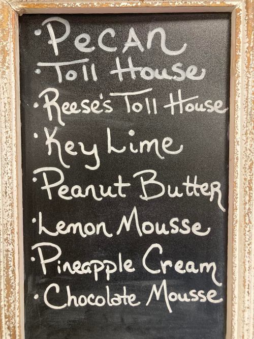 A chalkboard menu listing various dessert flavors: Pecan, Reese's Toll House, Key Lime, Peanut Butter, Lemon Mousse, Pineapple Cream, Chocolate Mousse.