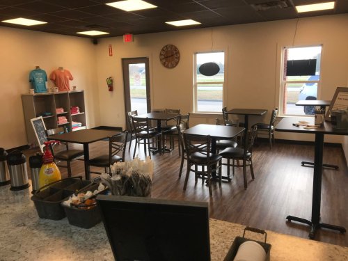 A cozy café interior with tables, chairs, and a counter, featuring a clock and merchandise on display.