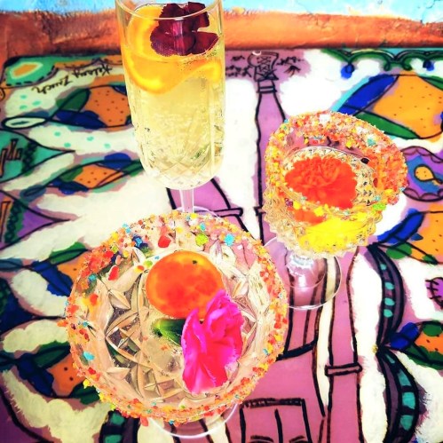 Three colorful cocktails with floral garnishes on a vibrant, patterned table.