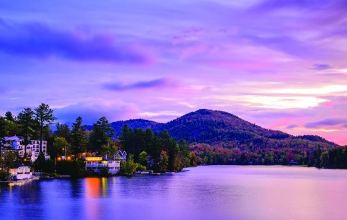 A serene lake at sunset, surrounded by trees and mountains, with colorful skies reflecting on the water.