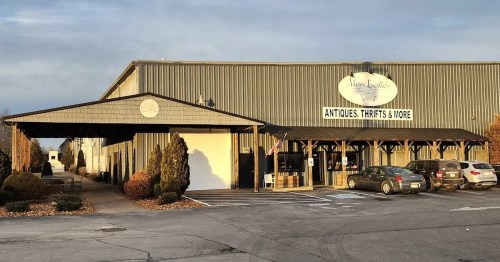 Exterior of a large building with a sign for "Miss Liddell's" featuring antiques and thrift items, surrounded by trees.