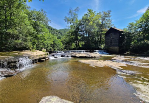A serene landscape featuring a waterfall, rocky shore, and a rustic wooden building surrounded by lush greenery.