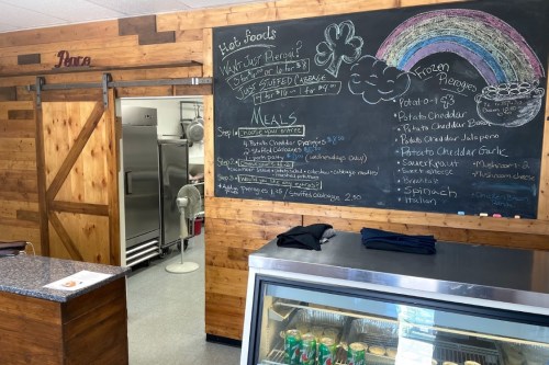 A cozy food counter with a chalkboard menu, showcasing meals and frozen pierogies, in a wooden interior.