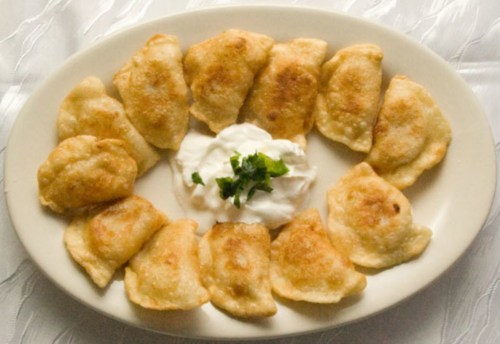 A plate of golden-brown fried dumplings arranged around a dollop of sour cream, garnished with fresh herbs.
