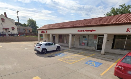 A parking lot with two cars in front of a storefront labeled "Mom's Pierogies" and a nearby building in the background.