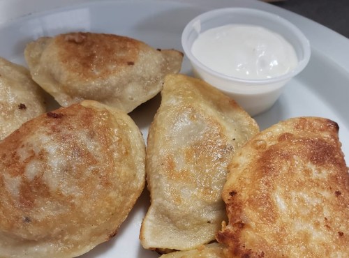 A plate of golden-brown fried dumplings served with a small cup of creamy dipping sauce.