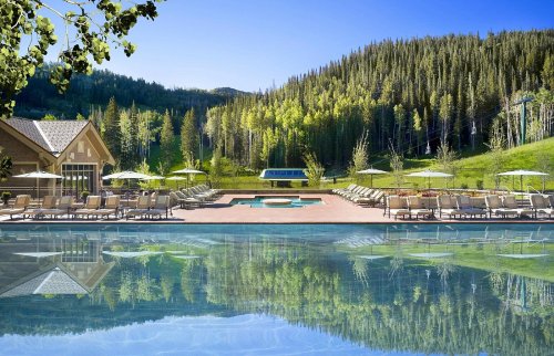 A serene pool area with lounge chairs, surrounded by lush green trees and mountains under a clear blue sky.