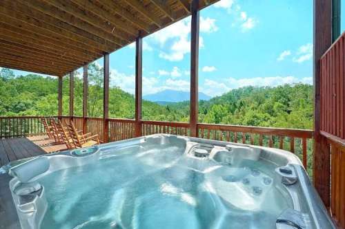 A hot tub on a wooden deck with a scenic view of green mountains and a blue sky in the background.