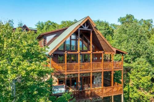 A large wooden cabin surrounded by trees, featuring multiple balconies and large windows.