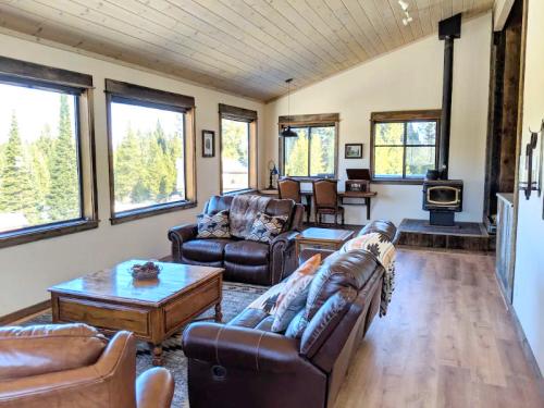 Cozy living room with large windows, wooden furniture, and a wood stove, surrounded by trees.