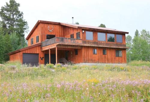 A rustic wooden house with large windows, surrounded by a colorful wildflower field and trees in the background.