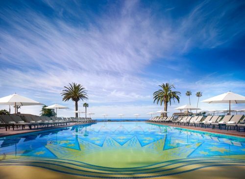 A serene pool with vibrant tile patterns, surrounded by lounge chairs and palm trees under a blue sky.