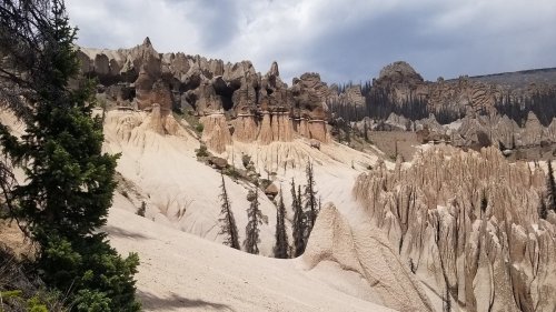 A rugged landscape featuring unique rock formations and sparse trees under a cloudy sky.