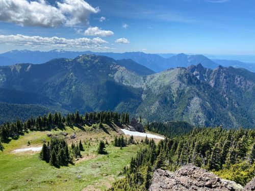 A panoramic view of lush green mountains under a blue sky with scattered clouds.