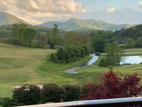 Scenic view of rolling green hills, a winding stream, and mountains under a partly cloudy sky.