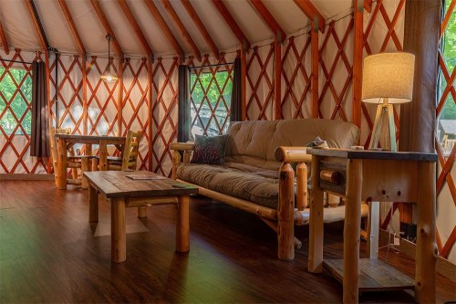 Cozy interior of a yurt featuring a sofa, wooden tables, and large windows with natural light.