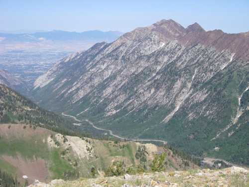 A panoramic view of rugged mountains with green slopes and a winding road below, under a clear blue sky.