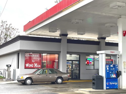 A gas station with a restaurant called "Chicken Wings by Wing Man" and a car parked at the pump.