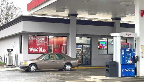 A gas station with a "Chicken Wings by Wing Man" sign and a parked car in front of the store.